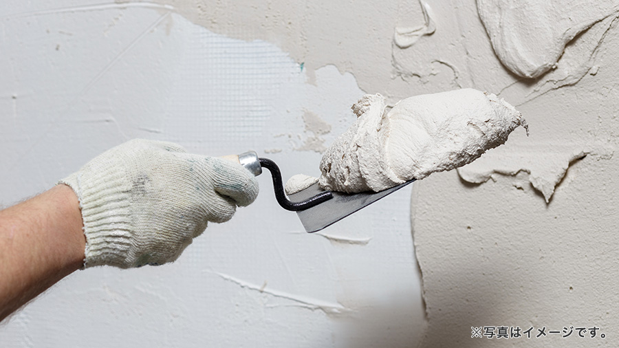 モルタルの壁に塗装をする職人の手